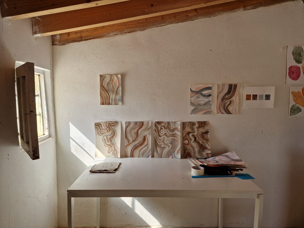 Residency studio wall with paintings in warm, natural light.